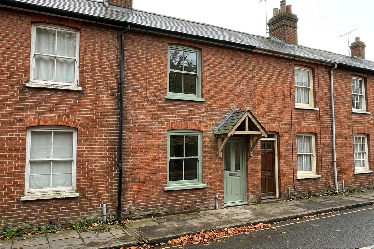 Red brick terrace with one house fitted with two sage green sash windows and a matching front door